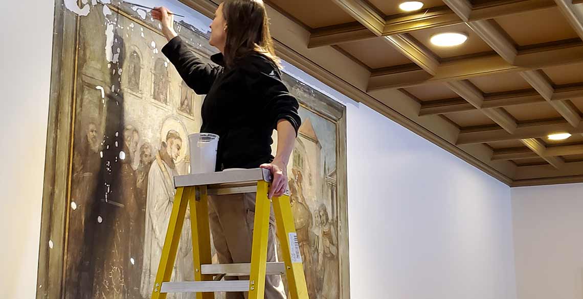 An art conservator works to restore a historic painting of St. Anthony of Padua inside the refectory of St. Francis of Assisi Monastery.