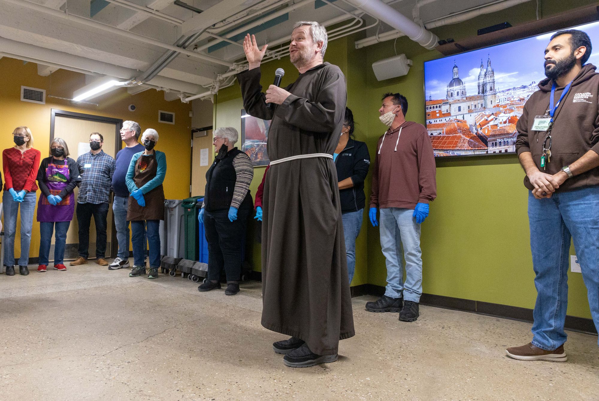 Br. Henryk Cisowski, wearing a brown Capuchin Franciscan habit and holding a microphone, offers the blessing before the meal at St. Ben's Community Meal.