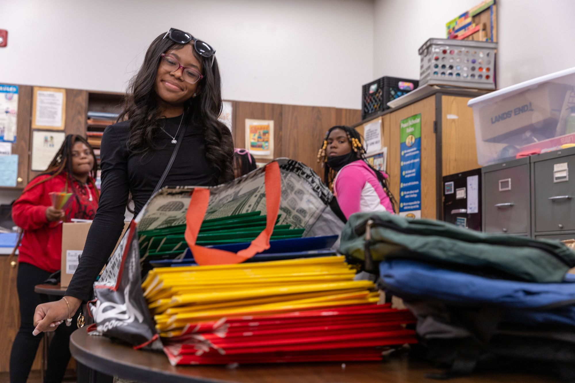 A color landscape photograph of a student volunteer taking a break from loading up backpacks with donated school supplies.