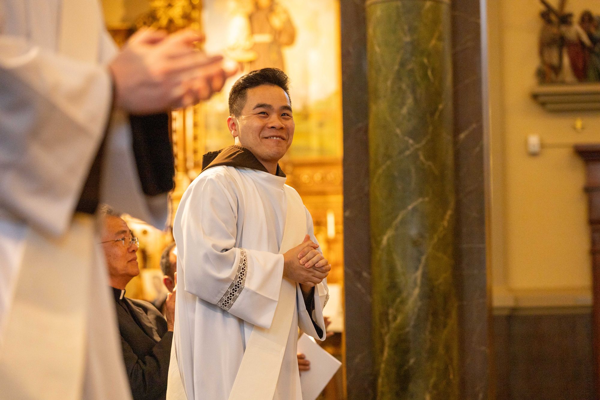 Color interior photograph of a smiling Br. Truong Tien Dinh, OFM Cap. in vestments at his ordination.