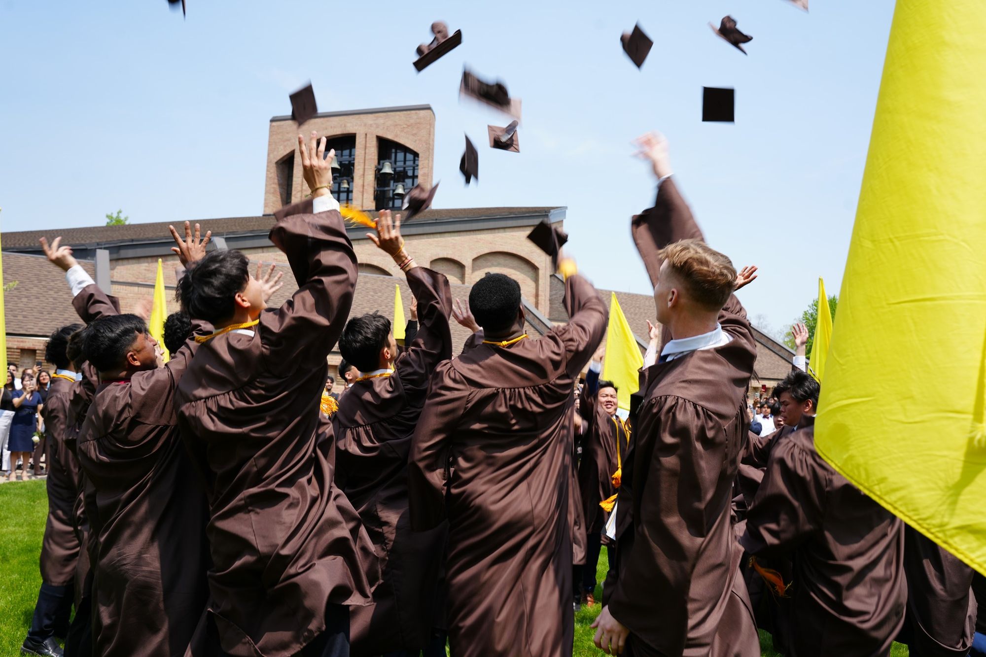 Photo of St. Lawrence graduates in the diag dressed in caps and gowns tossing their caps in the air after graduation.