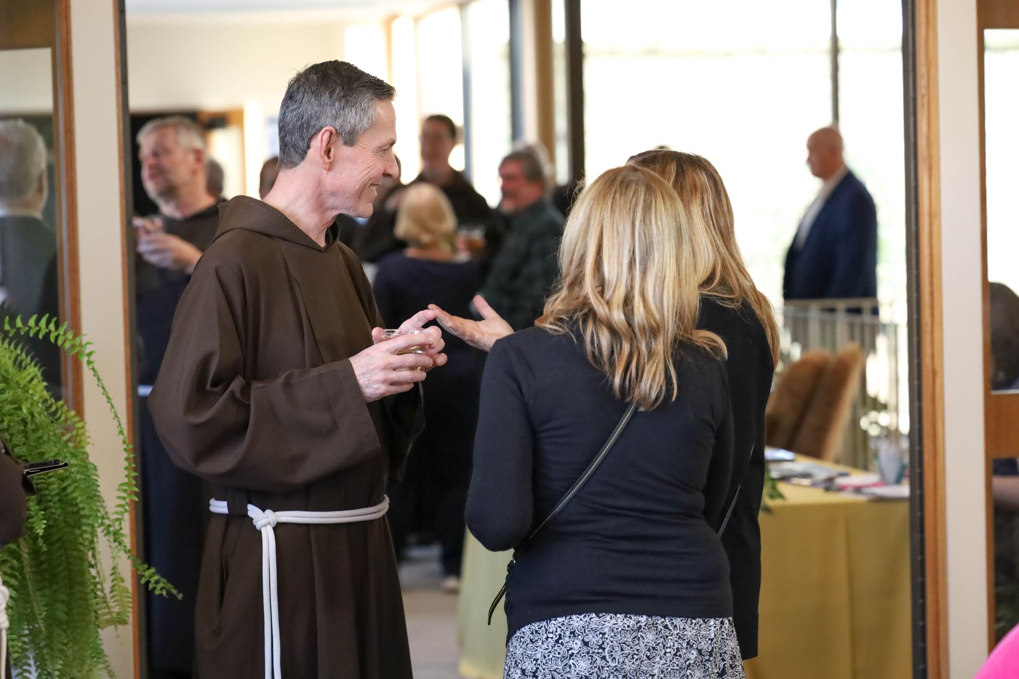 Color landscape photograph of Fr. Mike Bertram, OFM Cap. smiling in conversation with attendees of the Questors Club.