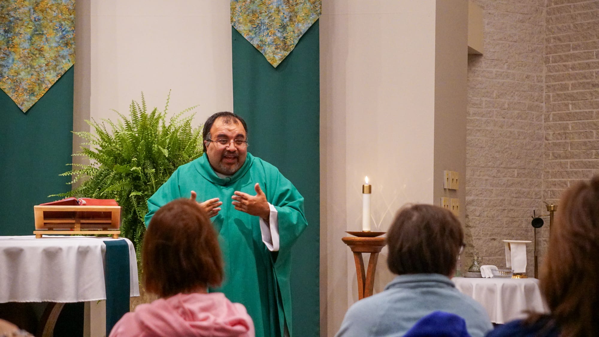 Fr. Vito, in green vestments, smiles while addressing the congregation as he delivers his homily.