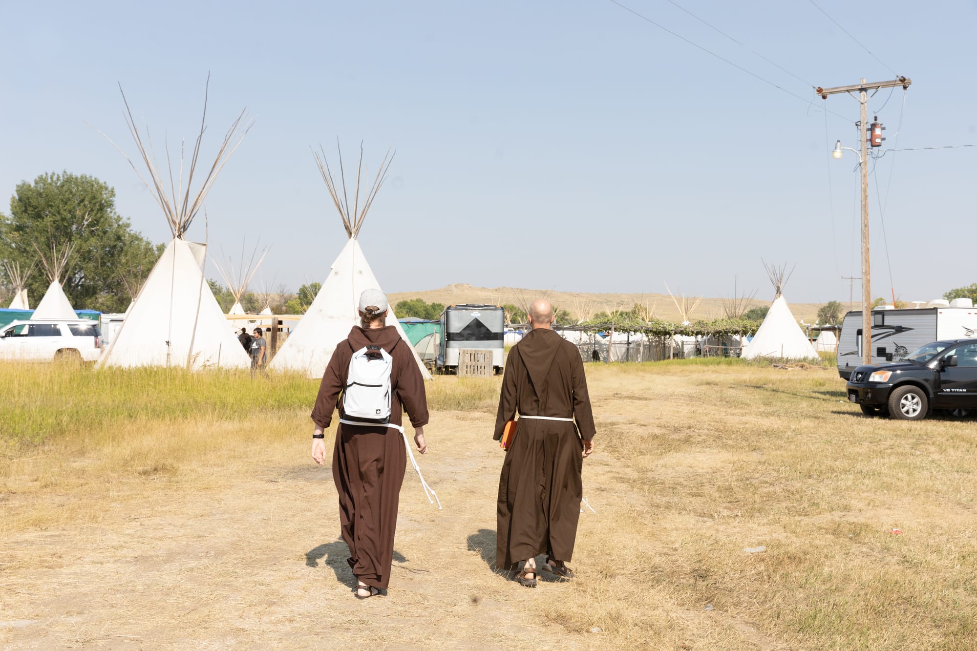 Two Capuchin friars in brown habits walking amidst white teepees.