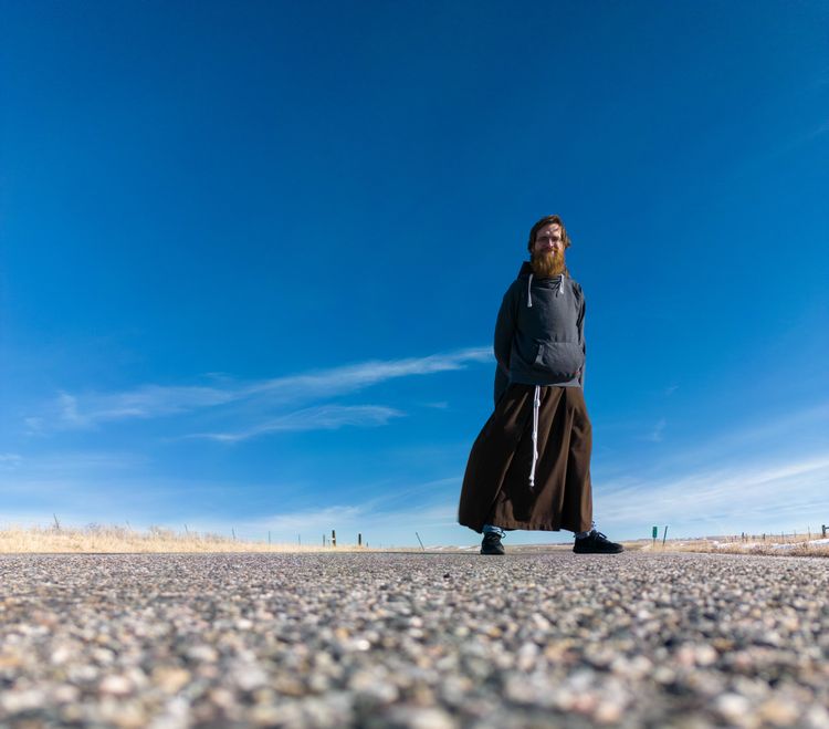 A low-angle photograph of Br. Thomas Skowron standing on blacktop with a very blue sky behind him.