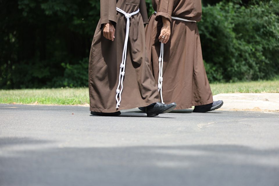 A cropped photo showing the lower half of two friars walking outside along a path.